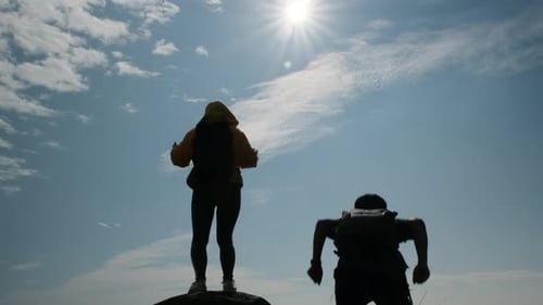 Silhouette of a successful Asian couple raising their arms on top of a mountain enjoying the valley.