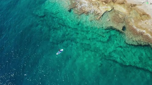 Sportler segelt SUP-Surfbrett entlang des Meeres, des felsigen Strandes