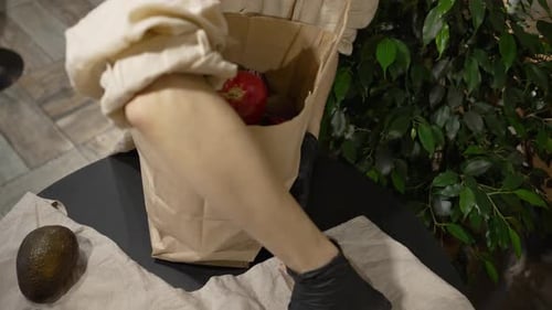 Mujer con guantes de goma negros pone verduras en bolsa de papel