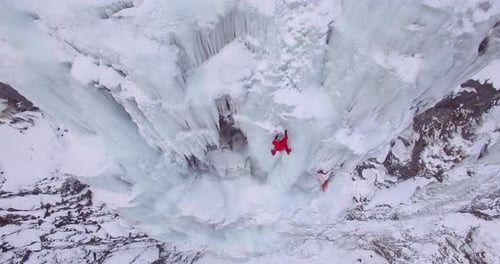Drohnenaufnahme eines Mannes, der auf einem gefrorenen Wasserfall in den Bergen eisklettert.
