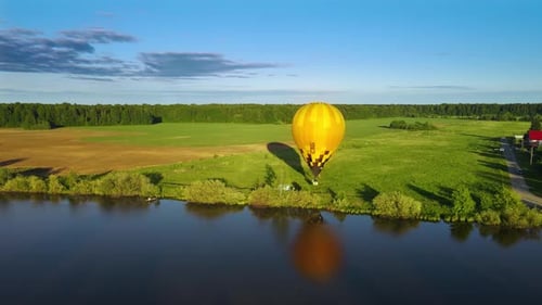 Yellow balloon rises slowly over river bank in ray of setting sun with aeronauts