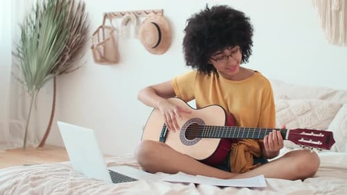 Young Woman Plays Guitar at Home with Laptop