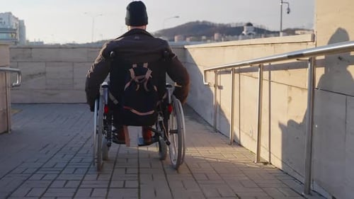 Adult Man in Wheelchair is Using Handicapped Ramp in Modern City for Moving