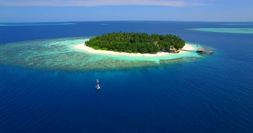 Aerial drone view of a man and woman sailing on a boat to a tropical island.