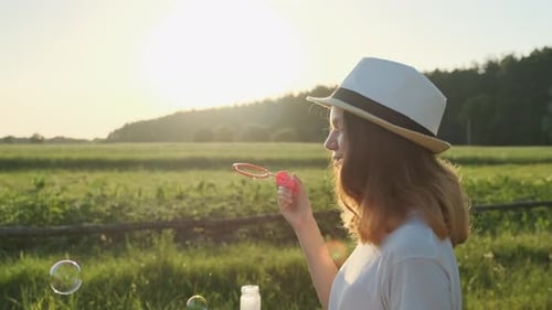 Young Woman Blowing Bubbles in a Green Field
