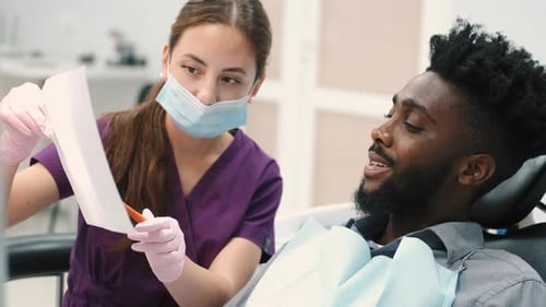 A Female Dentist Shows the Patient's X-ray of the Teeth and Discusses It