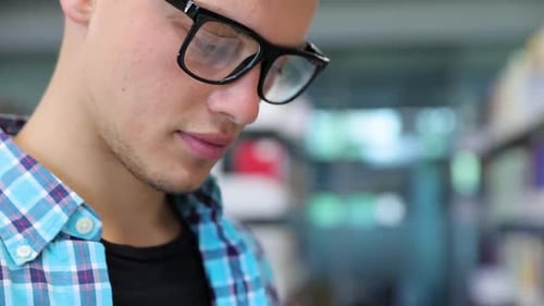 Buchhandlung. Männlicher Student liest Bücher in der Nähe von Bücherregalen