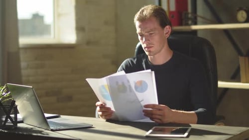 Hübscher konzentrierter junger Geschäftsmann, der am Schreibtisch sitzt und mit Dokumenten arbeitet