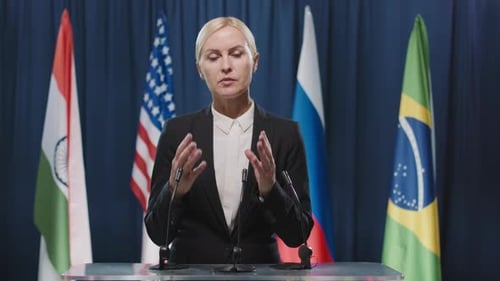 Woman Giving Speech in Front of Flags