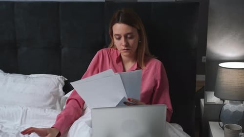 Woman Working with Laptop and Paperwork in Bed