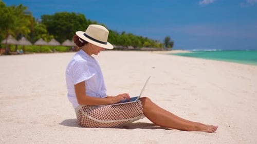 Business Woman in Yellow Hat Using Laptop Computer on the Background of a Tropical Beach with