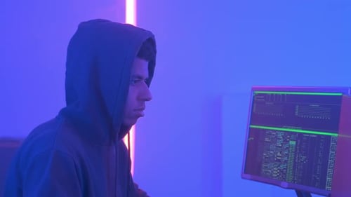 Profilansicht eines afrikanischen Hackers im Hoodie bei der Arbeit in einem mit Bildschirmen gefüllten Raum