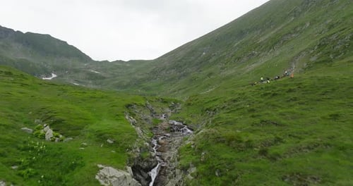 flying over a river in mountains in valley with tourists and hikers on background