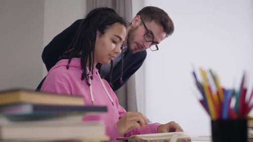 Porträt eines jungen kaukasischen Tutors in Anzug und Brille, der afroamerikanischen Studenten hilft