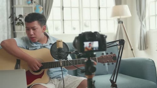 Un chico con guitarra dice algo y busca un comentario en una computadora portátil. El chico está transmitiendo