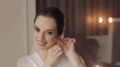 Young Woman Puts on Earrings in Preparation for Wedding