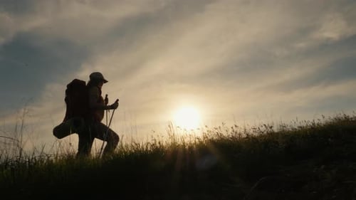 A Woman with a Backpack Climbs the Mountain at Sunset