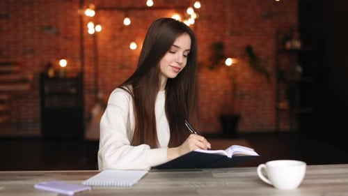 A Woman is Sitting in Her Home Office and Making Notes in a Notebook