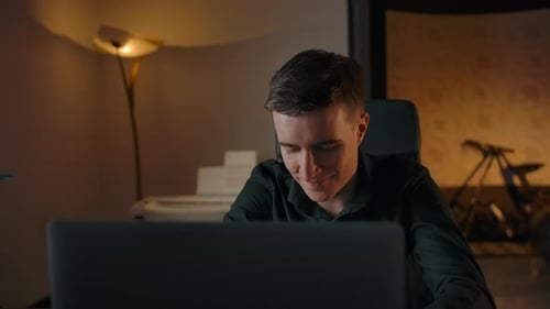 Young Man Uses Laptop at Desk in Evening