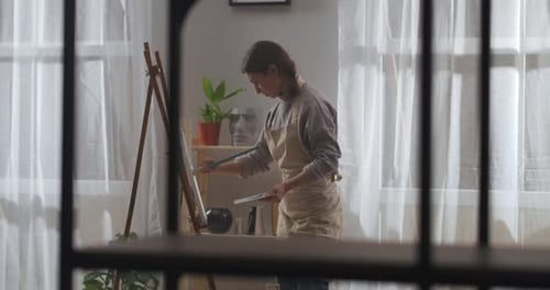 Home Studio of Young Female Painter Woman Is Drawing Picture on Canvas in Living Room of Apartment