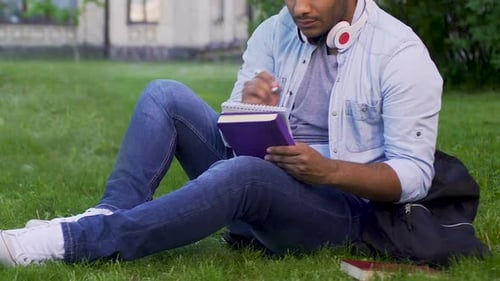 Universitätsstudent sitzt auf Gras, schreibt Essay, literaturwissenschaftliches Projekt