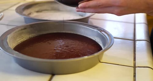 Un chef dans la cuisine verse la pâte à gâteau au chocolat végétalienne dans un plat de cuisson rond pour la mettre au four
