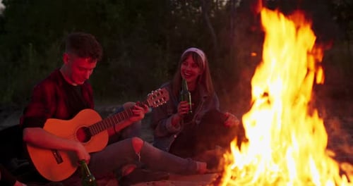 Friends Gather Around Campfire at Night with Guitar