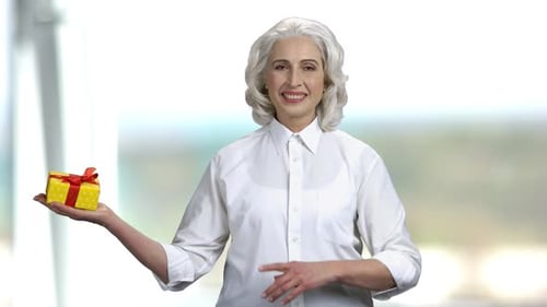 Senior Woman Holding Yellow Gift Box and Pointing