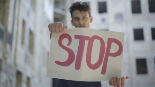 Rack Focus Goes To STOP-Banner, das von einem seriösen jungen Mann in Slums Porträt von Konzentrierter Mischung