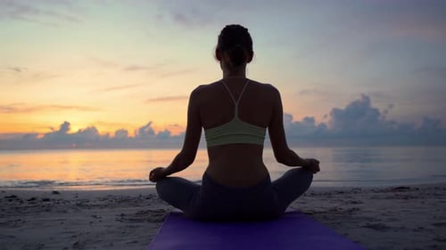Woman meditating at beach sunset or sunrise relaxing in yoga pose