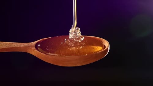 Honey Dripping From a Wooden Honey Dipper on Black, Back Violet Light