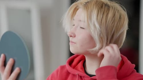 Nahaufnahme eines selbstbewussten asiatischen Teenagers, das Make-up anpasst und Haare in den Handspiegel schaut