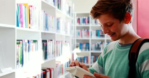 Smiling schoolboy using digital tablet in library