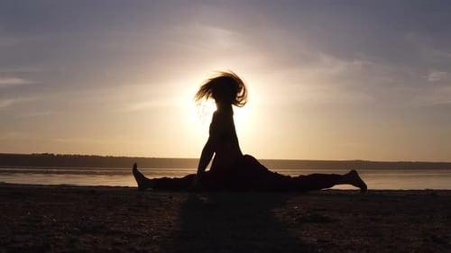 Mujer joven haciendo una postura de yoga dividida al aire libre en la playa