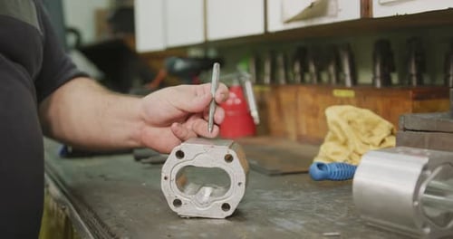 Kaukasischer Mann händet Fabrikarbeiter in einer Fabrik, der an einer Werkbank sitzt und an einem Metall arbeitet