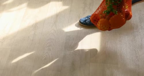 Mujer camina con zapatos verdes sosteniendo una bolsa de la compra llena de frutas y verduras frescas en casa