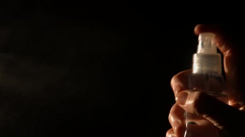 Hand Sprays Clear Bottle on Black Background