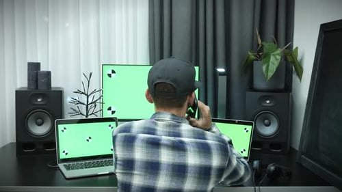 On the phone in front of green screen chroma key computer monitors
