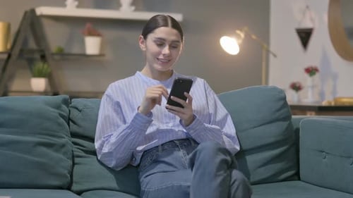 Young Woman Using Mobile Phone on Couch Indoors