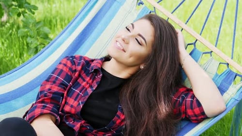 Close-up Portrait of a Beautiful Happy Girl Lies on a Hammock in the Garden, Smiles and Relaxes