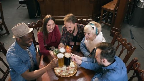 Friends Toasting Drinks Around a Pizza in Pub