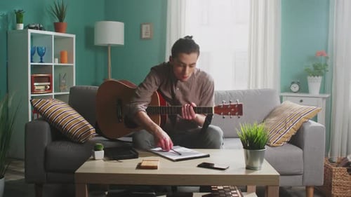 Young Adult Playing Guitar and Songwriting at Home