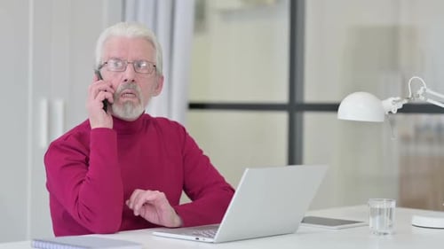 Alter Mann mit Laptop spricht auf Smartphone
