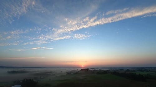A slow aerial shot of a sunrsie over the field and village in the fog