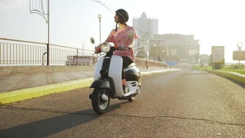 Junges schönes Mädchen fährt bei Sonnenaufgang mit dem Roller durch die Stadt