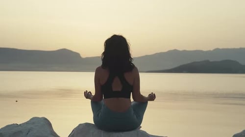 Girl Meditates in a Yoga Pose By the Ocean at Sunset