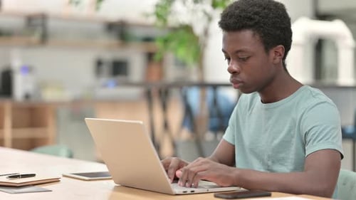 Focused Young Adult Typing on a Laptop Indoors