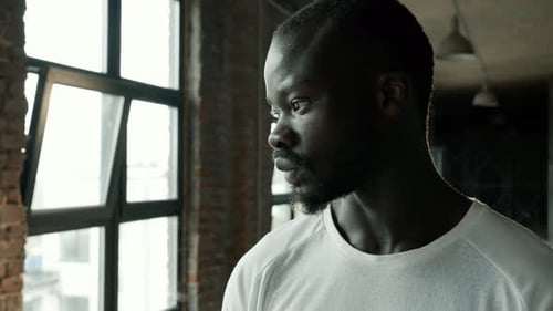 Young Man Looking Out Window in Urban Apartment