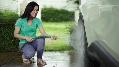 Woman Washes Car Tire with Hose