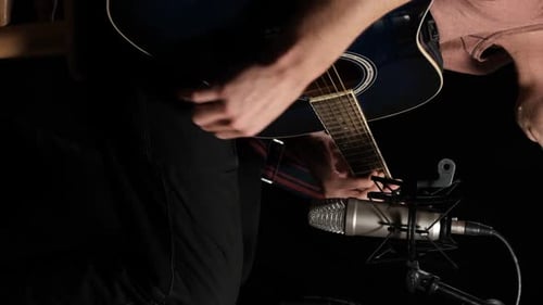 Vertikales Video. Junger Mann spielt eine Akustikgitarre auf schwarzem Hintergrund
